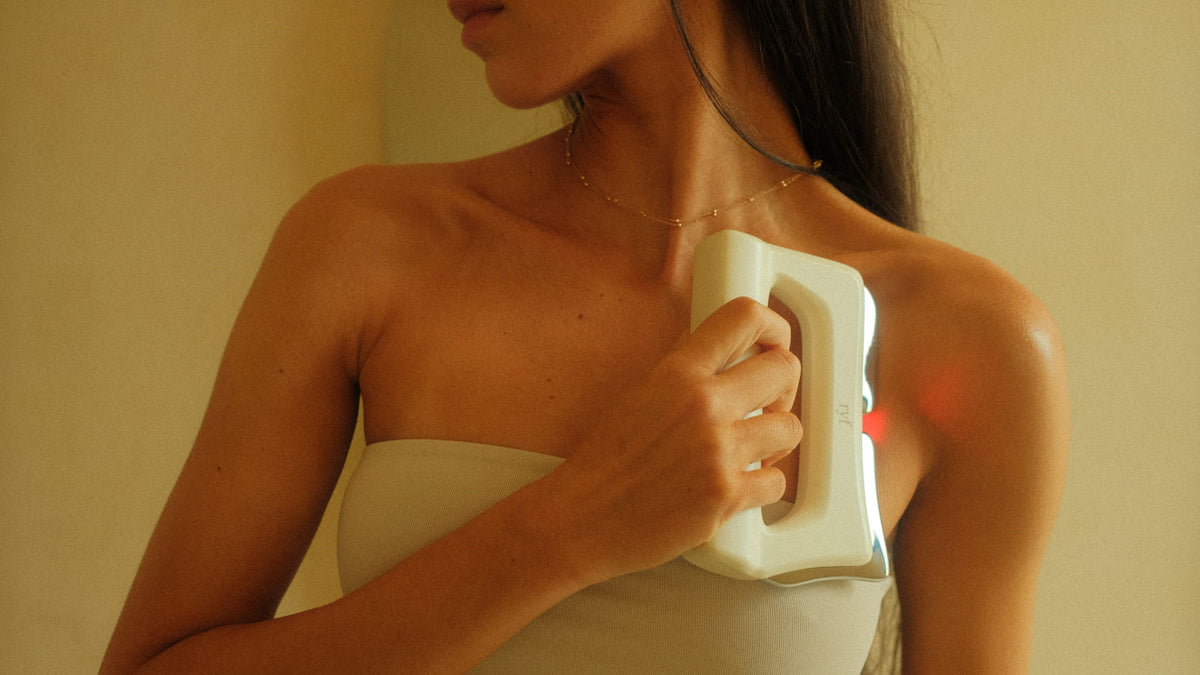 A woman holding FasciaWave against her shoulder, its red light glowing